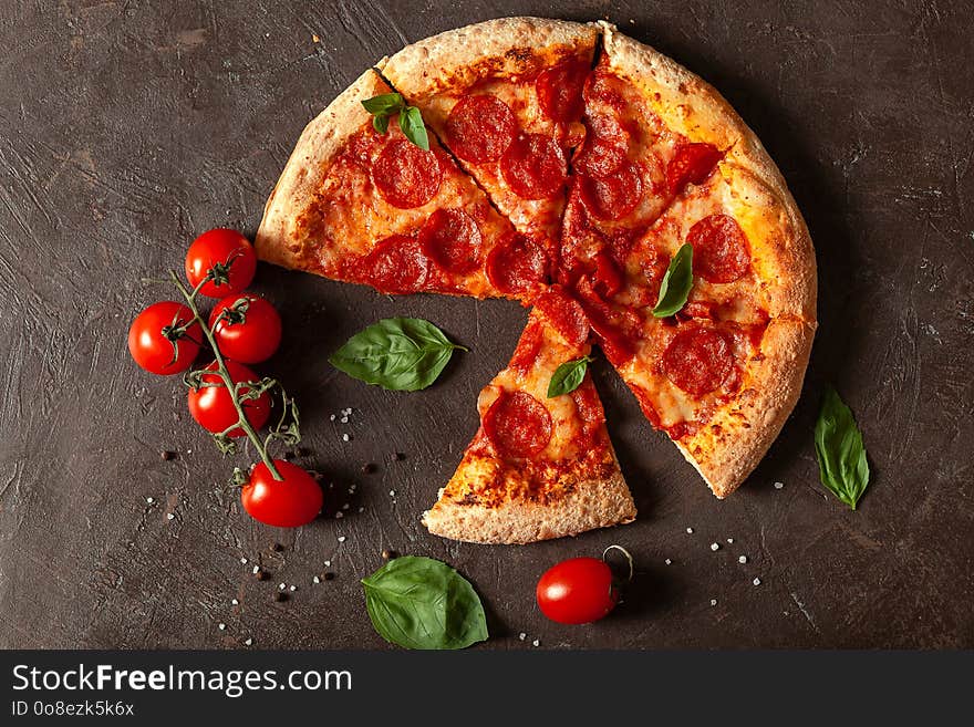 Pizza Pepperoni, pizza ingredients, tomatoes, Basil, spices on a brown concrete background. Pizza place, fast food. The view from the top. With copy space for text. Flat lay