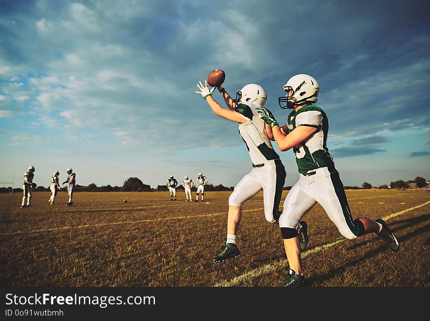 American football player receiving a pass during team practice drills on a football field against a moody afternoon sky. American football player receiving a pass during team practice drills on a football field against a moody afternoon sky