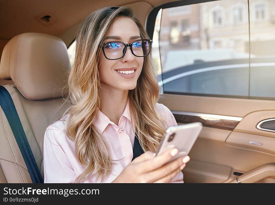 Attractive businesswoman holding smartphone and looking away in the car