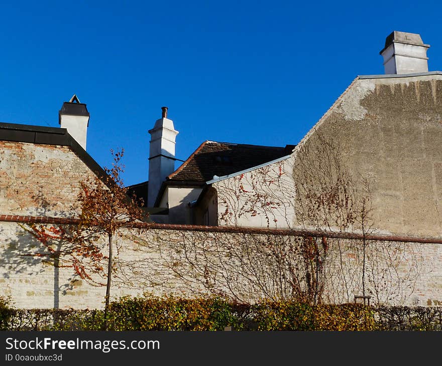 Chimneys and flat brick fire walls along the public Belvedere Garden in Vienna under blue sky on a bright November day with small yellow trees and vine climbing on brick walls. concept of tourism. Chimneys and flat brick fire walls along the public Belvedere Garden in Vienna under blue sky on a bright November day with small yellow trees and vine climbing on brick walls. concept of tourism