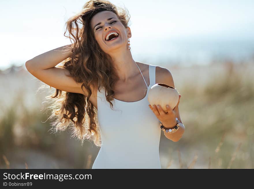 Happy Young Woman With Coconut Adjusting Hair On Ocean Shore