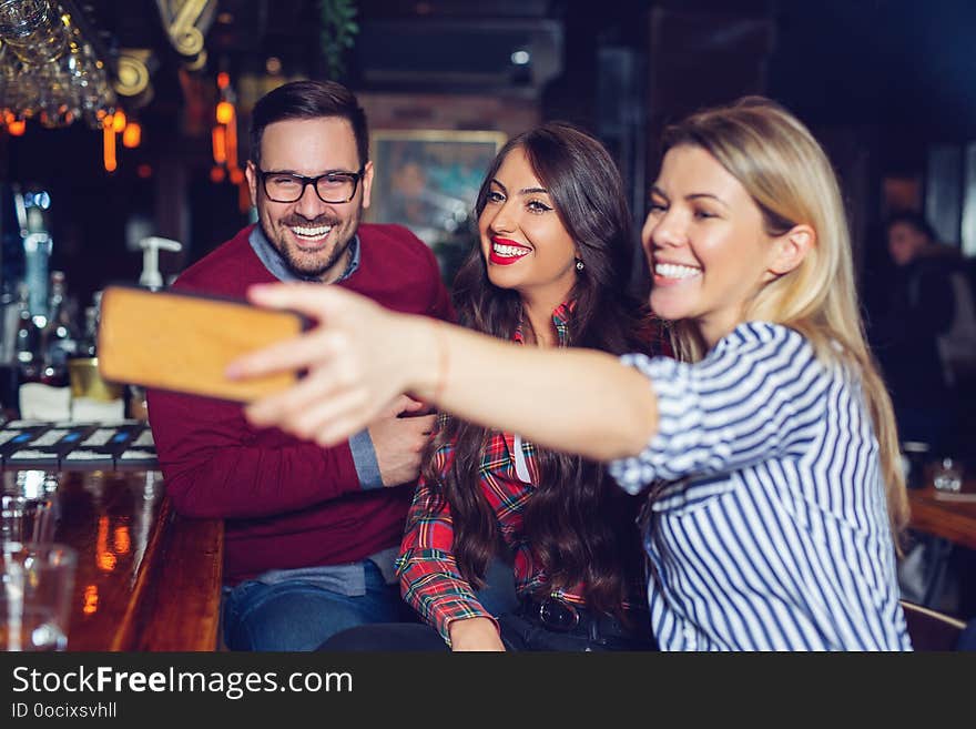 Young beautiful three friends taking selfie in a bar. - Image