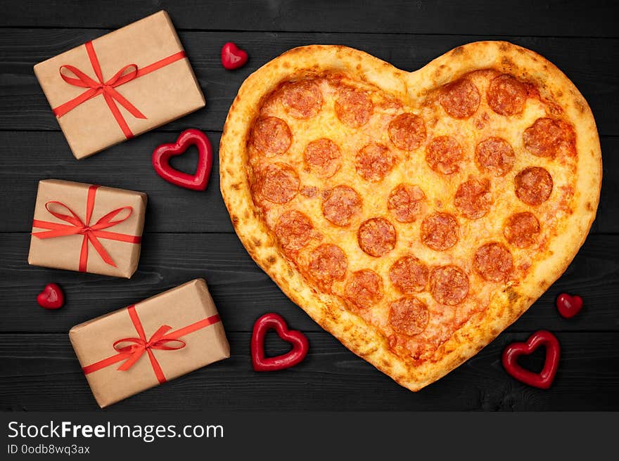 Pizza shaped heart with gift box for Valentine`s Day romantic concept on rustic dark black background. Top View. Flat lay.