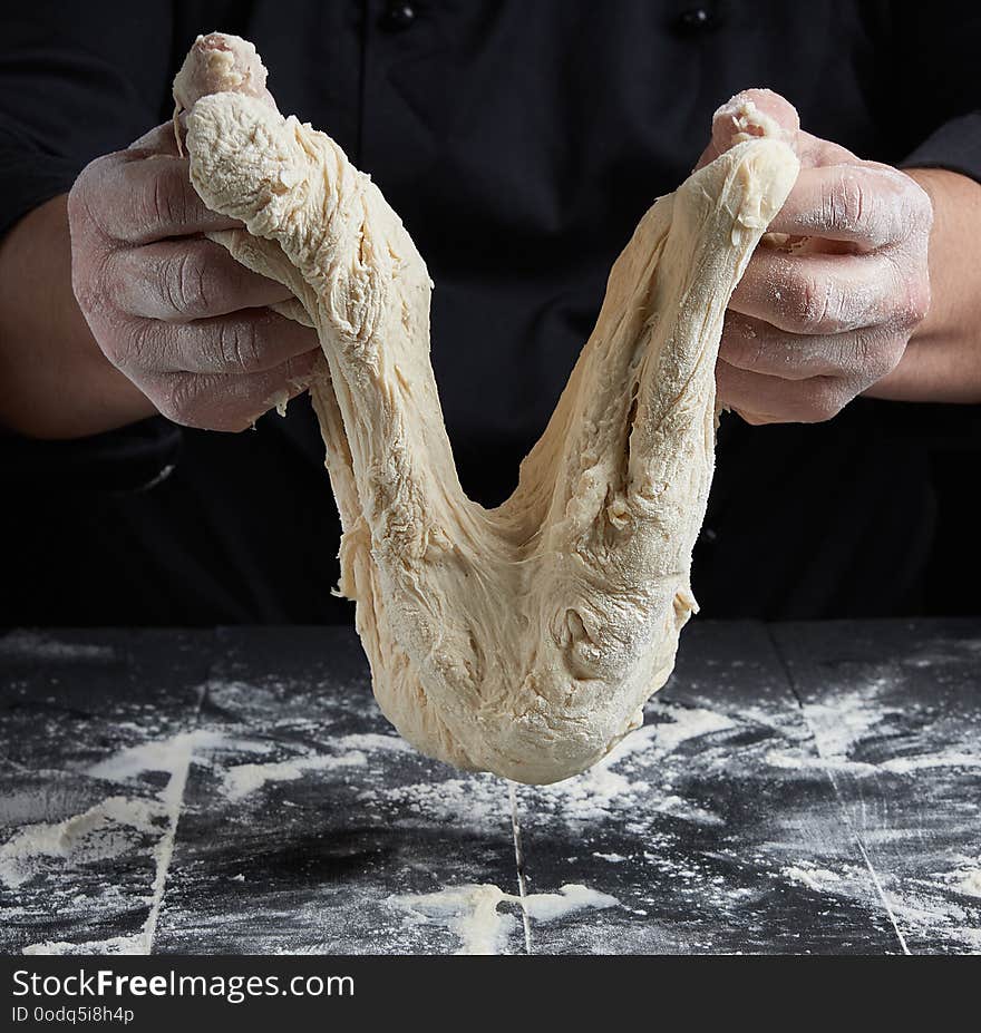 Cook stretches kneaded dough from white wheat flour over a black wooden table