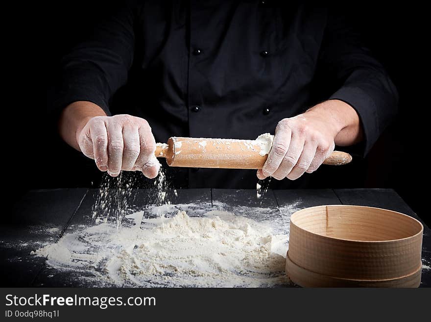 Wooden rolling pin in men`s hands,white wheat flour scattered on the table