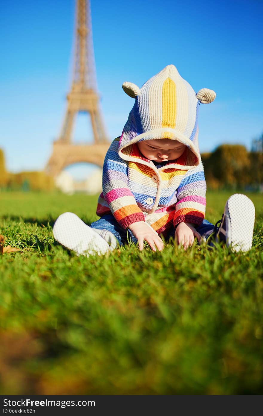 Baby girl sitting on the grass near the Eiffel tower in Paris, France