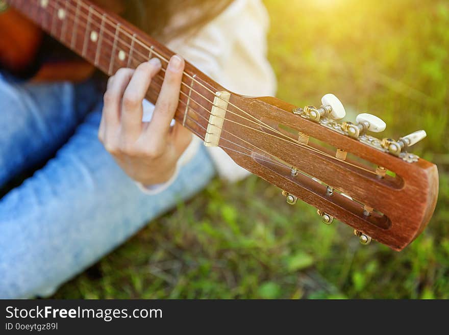 Closeup of woman hands playing acoustic guitar on park or garden background. Teen girl learning to play song and writing music. Hobby, lifestyle, relax, Instrument, leisure, education concept