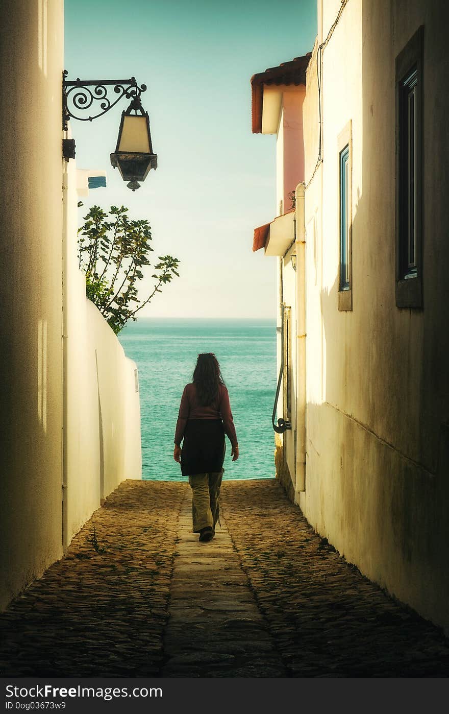 Woman walking away in an alley between houses into the sea. Woman walking away in an alley between houses into the sea