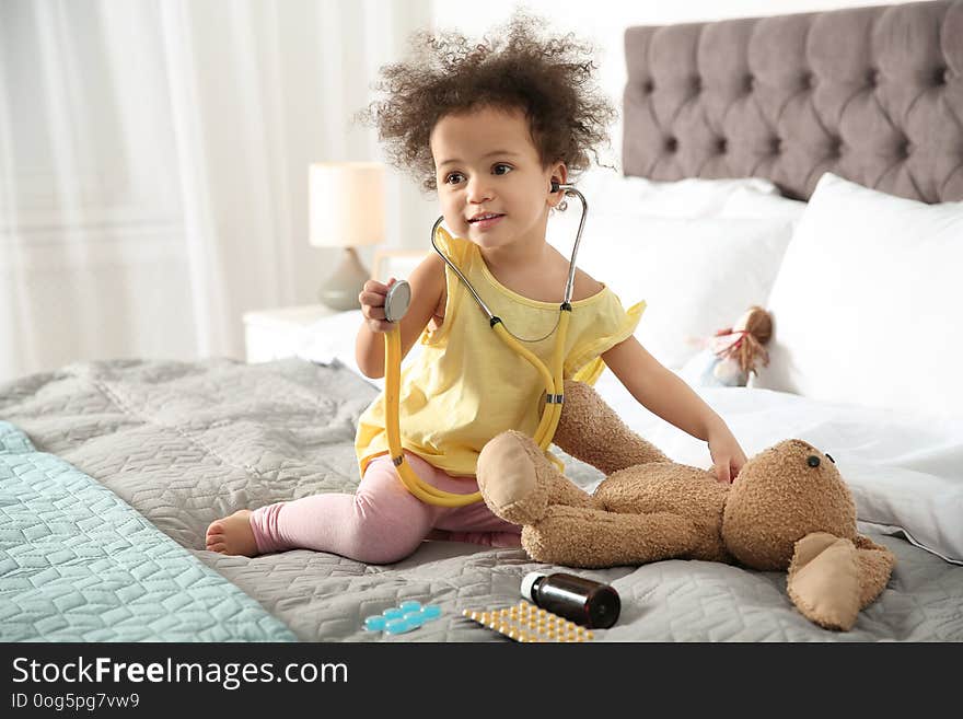 Cute African American child imagining herself as doctor while playing with stethoscope and toy bunny