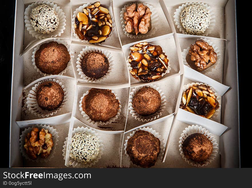 top view on big handmade box filled with assorted healthy useful handmade candies decorated with caramelized sunflower and pumpkin seeds, cocoa powder, walnut and sesame seeds on black mirror background