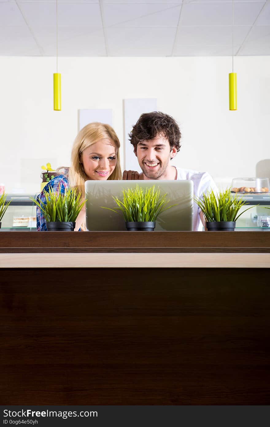 A beautiful young couple sitting in a coffee shop and using a laptop. A beautiful young couple sitting in a coffee shop and using a laptop