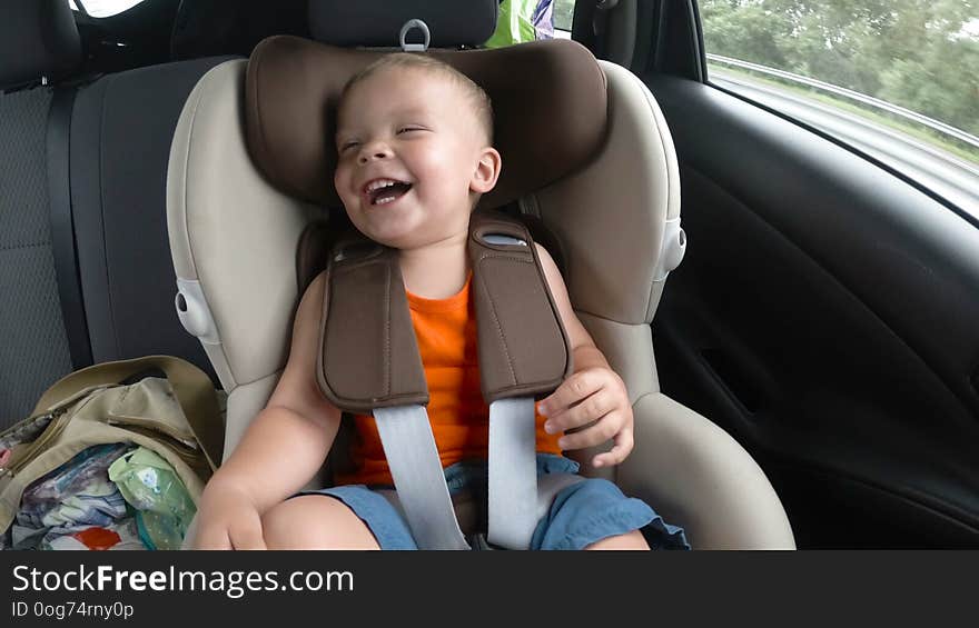 Baby boy in the children`s car seat in the car. Kid smiles, laughs and waves his hands happily.