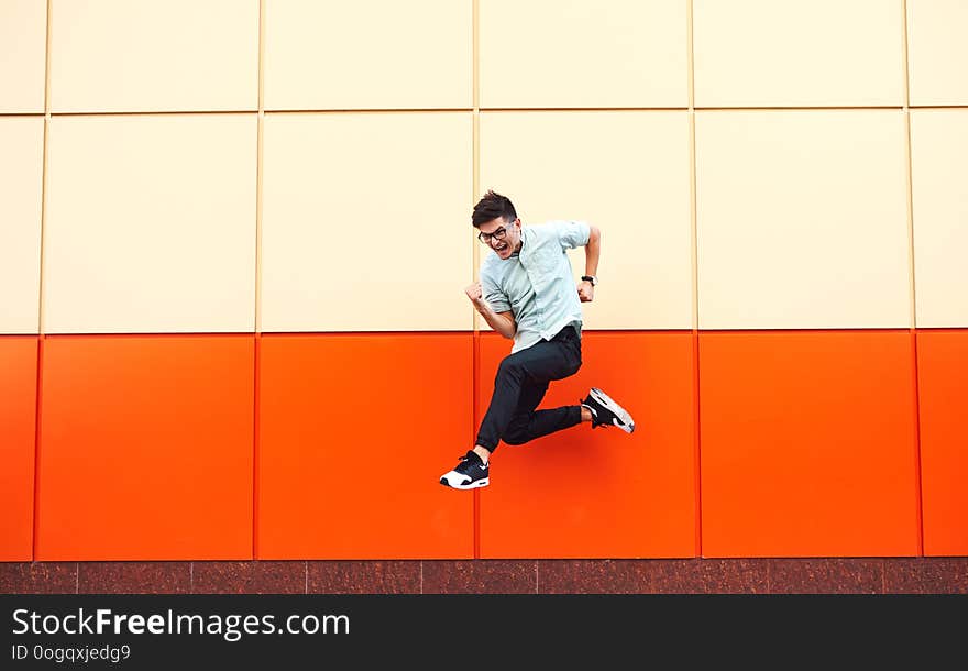 Handsome young man in modern clothes jumping against the orange wall. Handsome young man in modern clothes jumping against the orange wall.