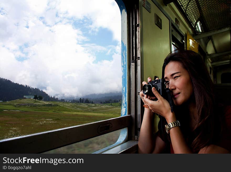 Young beautiful Asian woman wearing sunglasses traveling by train sitting near the window and looking through the train window. Young beautiful Asian woman wearing sunglasses traveling by train sitting near the window and looking through the train window.