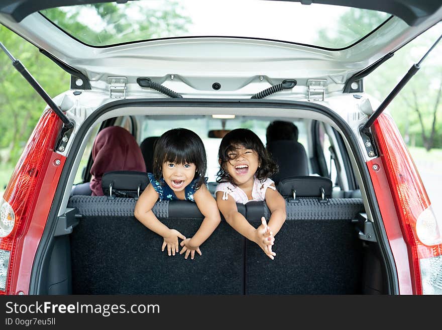 Two daughter playing in the car back seat and look back from baggage