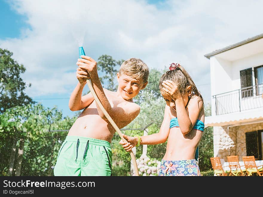 Hot Summer Days Activity: Happy Little Girl Jumps Under Water, When Brother Pours Her From Garden Hose