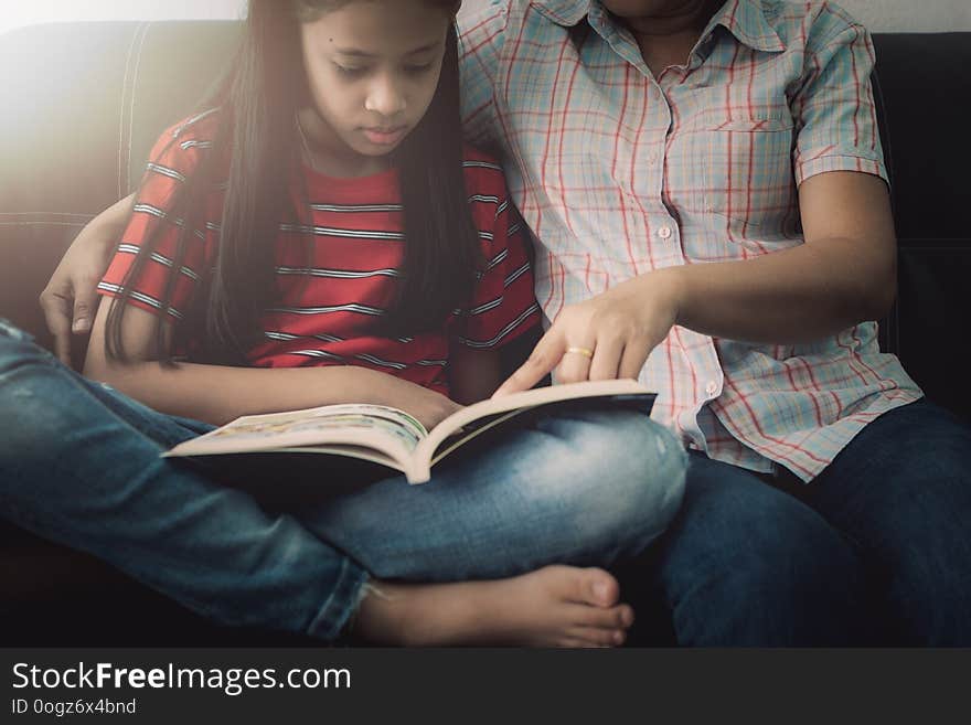 Mother and daughter reading book and having fun while spending time together at home under the warm light