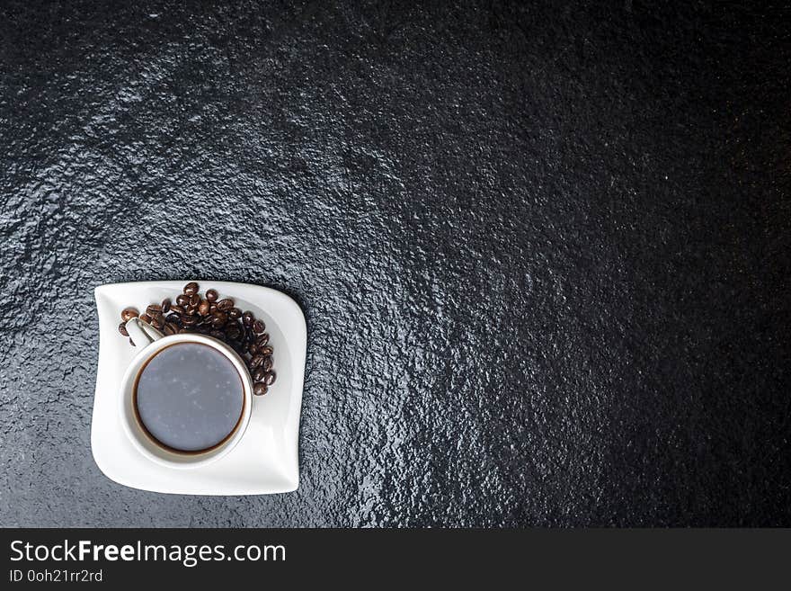 White cup of coffee and coffee beans on black stone table top view