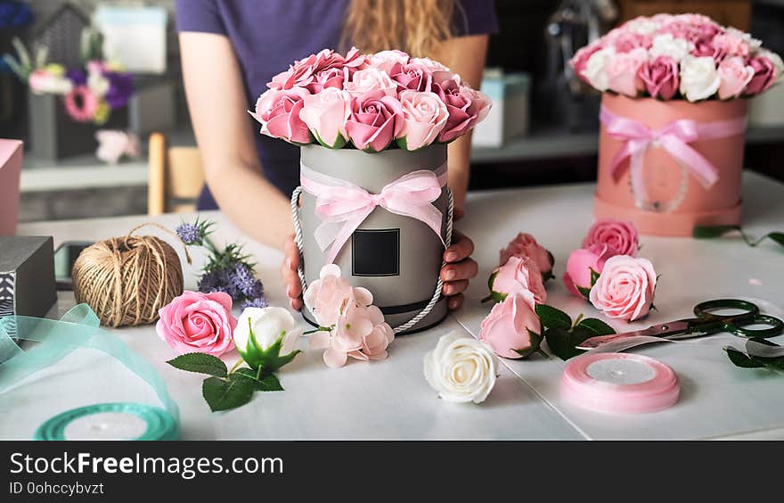 Flower Shop: A Florist Girl Collects A Bouquet In A Round Box Of Pink Roses. Blond Curly Hair, Gray Background.