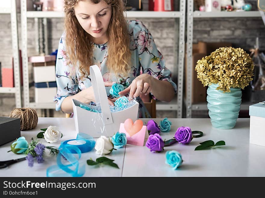 Flower shop: florist girl collects a bouquet of red roses in a blue paper basket.