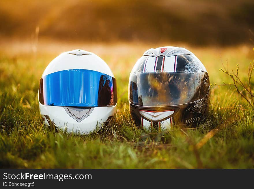 Two motorcycle helmets lie on the grass in the sun.