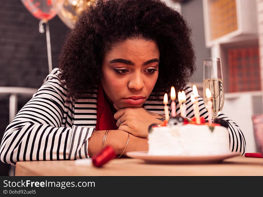 Being lonely. Cheerless young woman thinking about her life while looking at the candles on the birthday cake