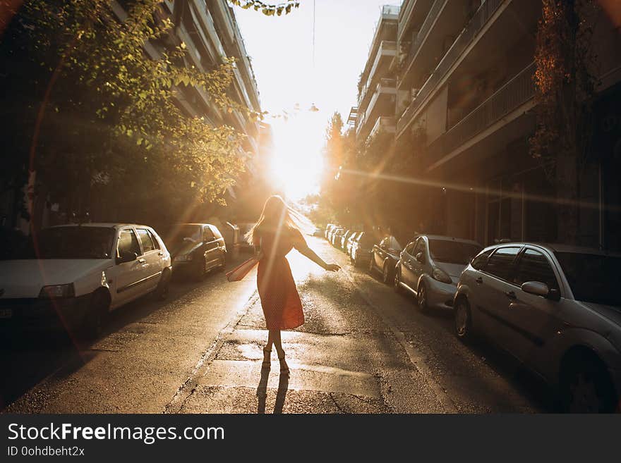 Girl in dress city street between cars at sunset with sun rays. Girl in dress city street between cars at sunset with sun rays