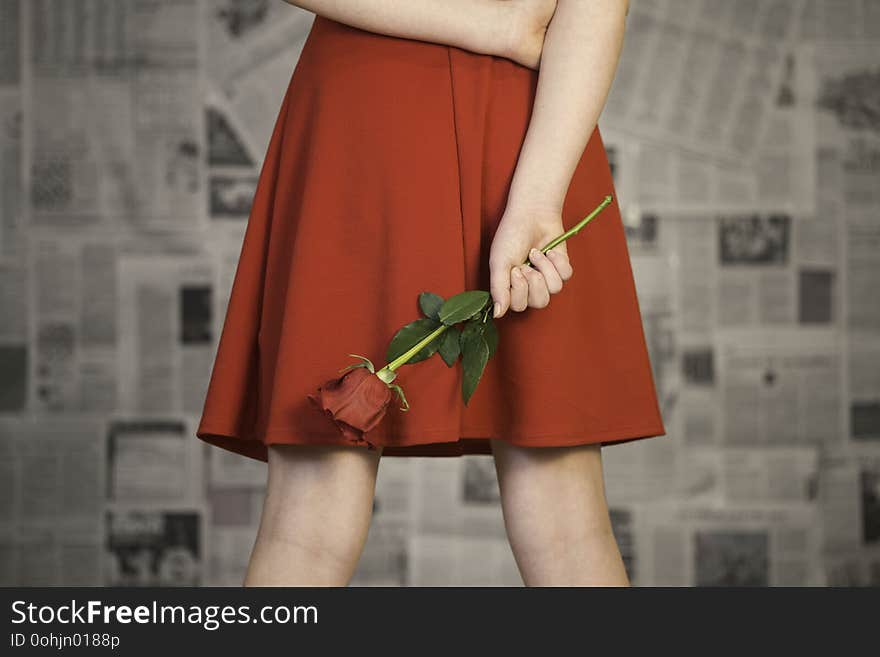 Female wearing red dress holding a rose behind her back