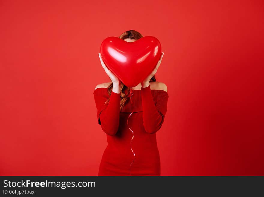 Young charming girl with long blonde curly hair, in red dress holding air balloons, posing at camera. St. Valentine`s day. Young charming girl with long blonde curly hair, in red dress holding air balloons, posing at camera. St. Valentine`s day.