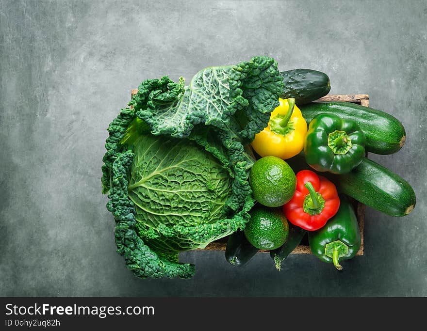 Assortment of organic green red yellow raw vegetables savoy cabbage cucumbers zucchini avocado capsicums in wood box