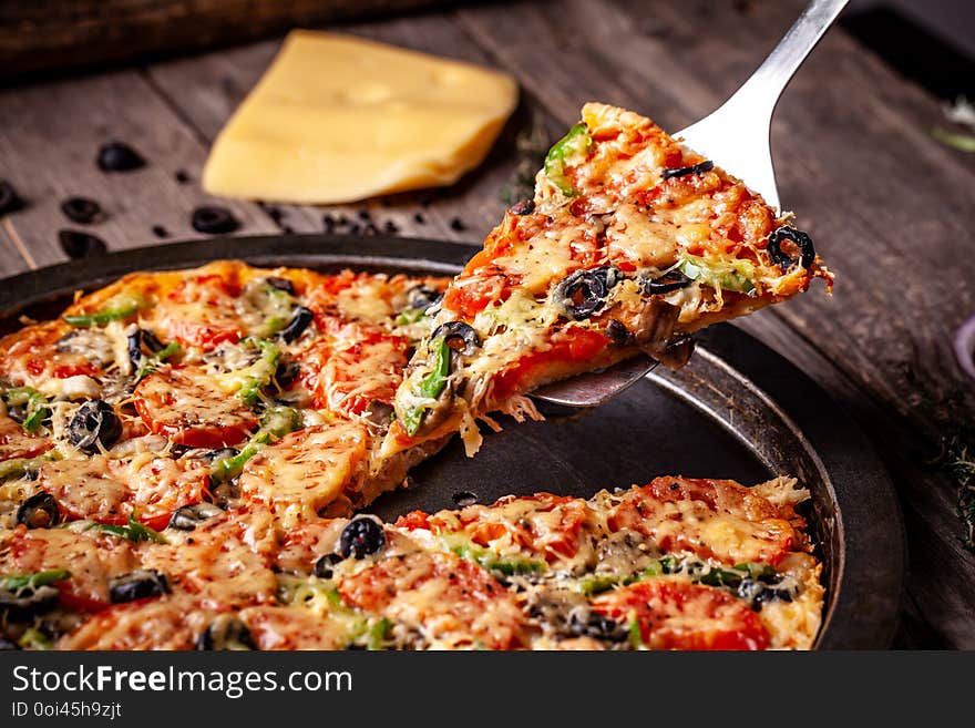 Concept of Italian cuisine, Homemade Italian pizza with salami sausage, tomatoes, with black olives and cheese on a wooden background. copy space