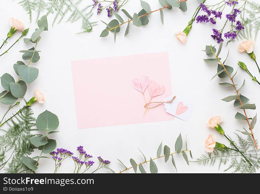 Flowers composition. Paper blank, carnation flowers, eucalyptus branches on pastel background. Flat lay, top view, copy spaceFlat