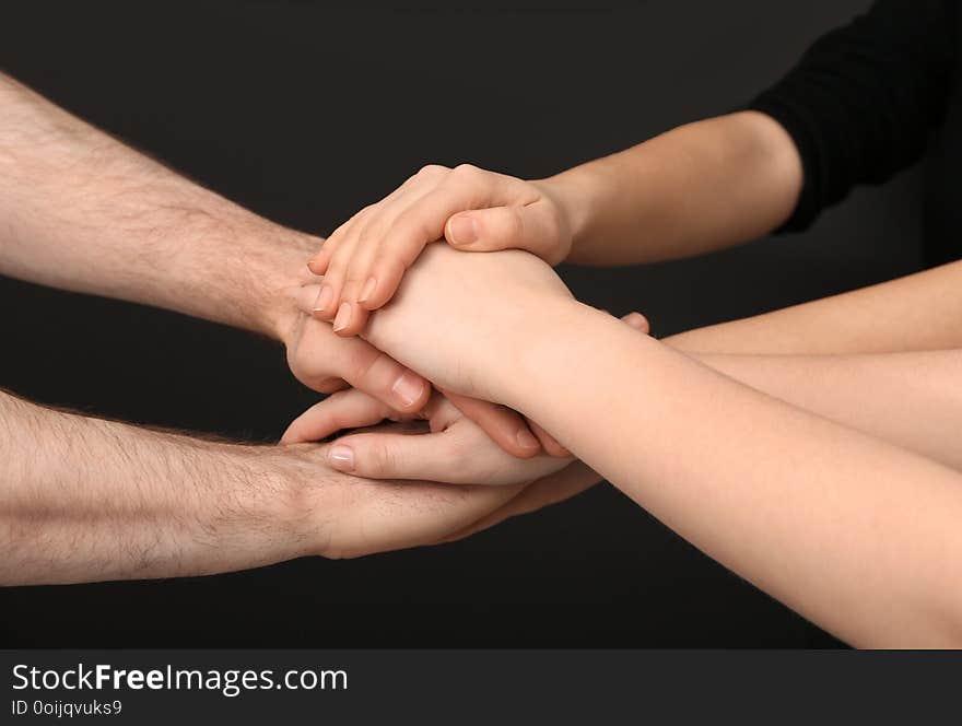 Young people putting their hands together on dark background