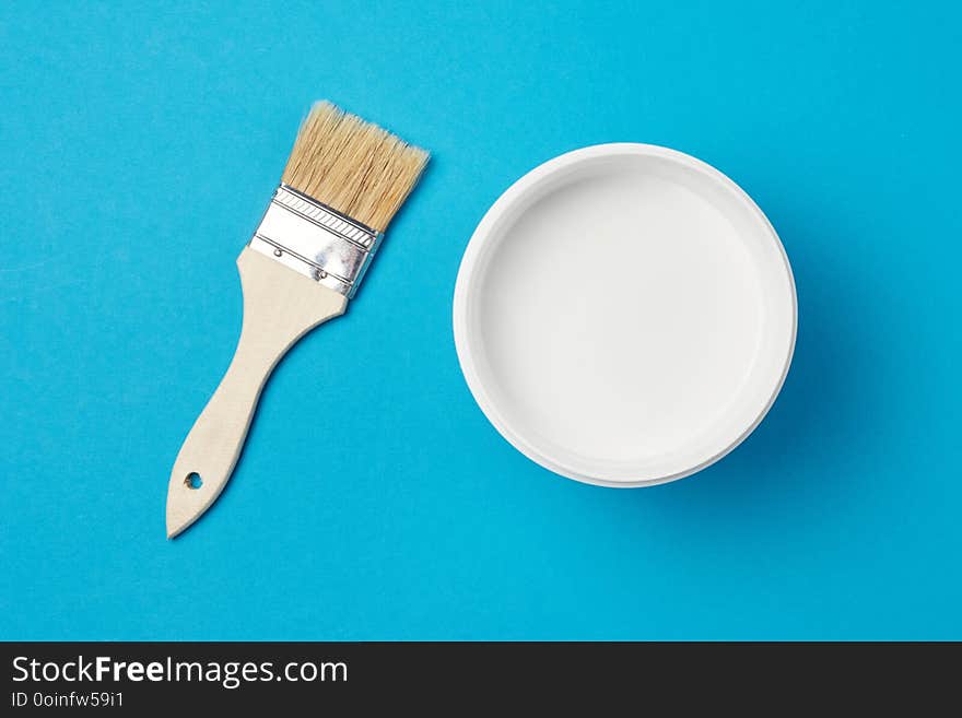 Brush and paint can with white color on a blue background, closeup