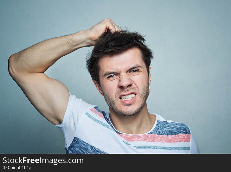 Portrait of frustrated young man pulling his hair on a gray wall background