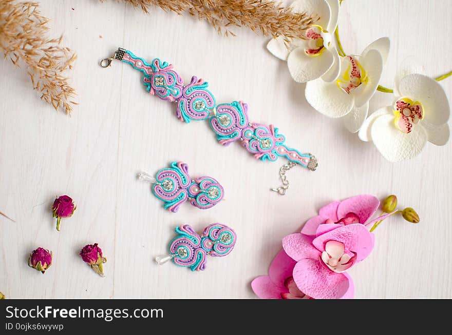 Beaded braselet and earrings set. Pink and blue soutache jewelry with flowers on the white wooden background. Women accessories.