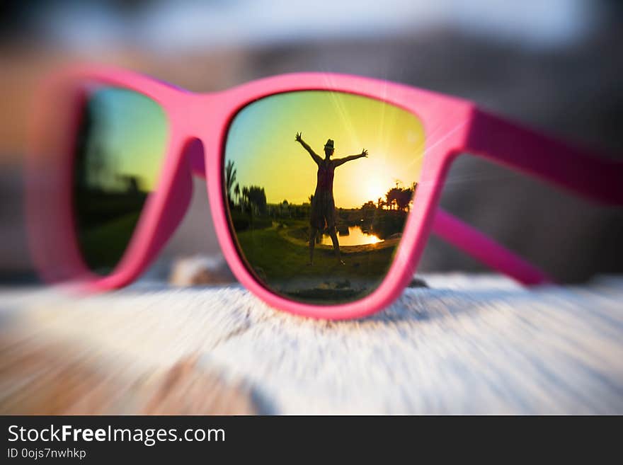 Excited girl with hands wide opened silhouette in the pink sunglasses reflection on a summer day and sunset. Excited girl with hands wide opened silhouette in the pink sunglasses reflection on a summer day and sunset