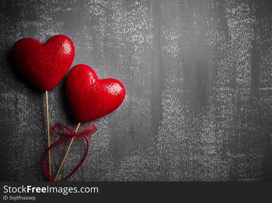 Valentines day and love concept. Two handmade red hearts with red ribbon on gray wooden background.