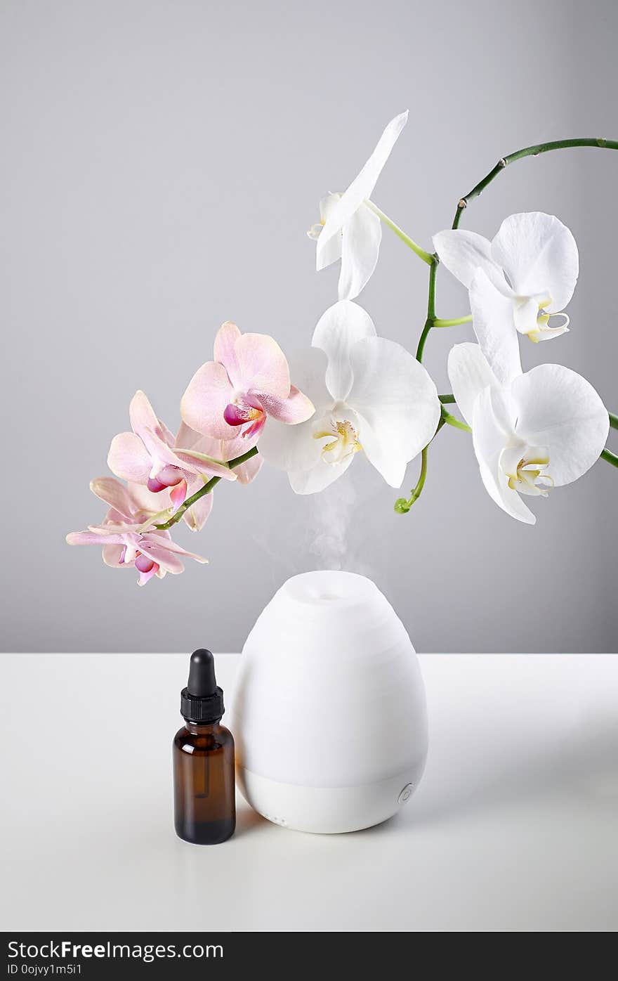 Oil diffuser with glass amber bottle and orchid flowers on white table