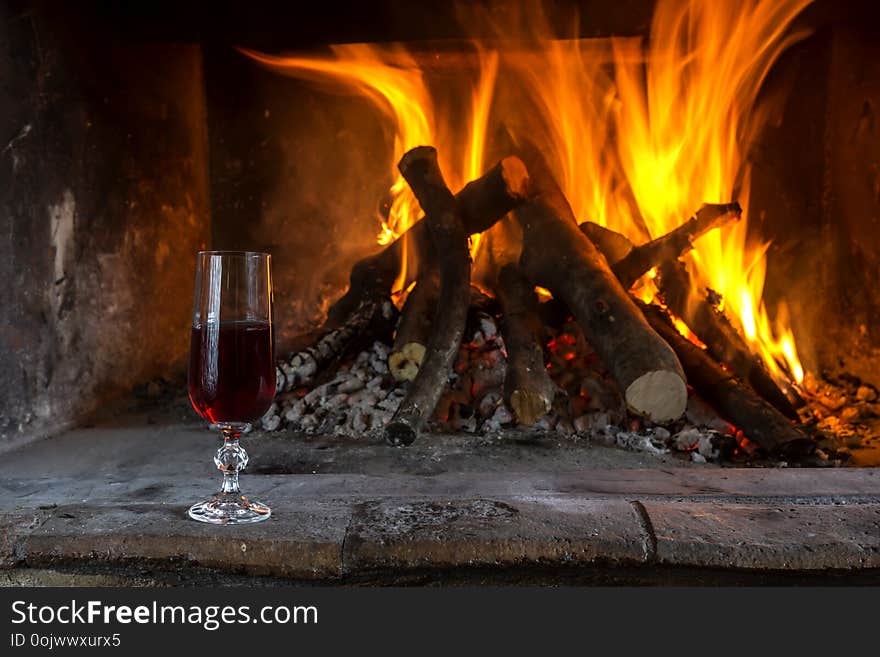 Burning fireplace in the winter season. The firewood burning in fireplace and a glass of wine close-up