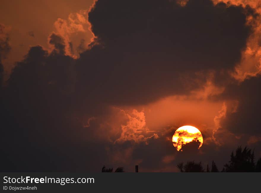 The orb of the rising sun burns white and gold against an orange sky. Dark clouds fill the sky. The orb of the rising sun burns white and gold against an orange sky. Dark clouds fill the sky.