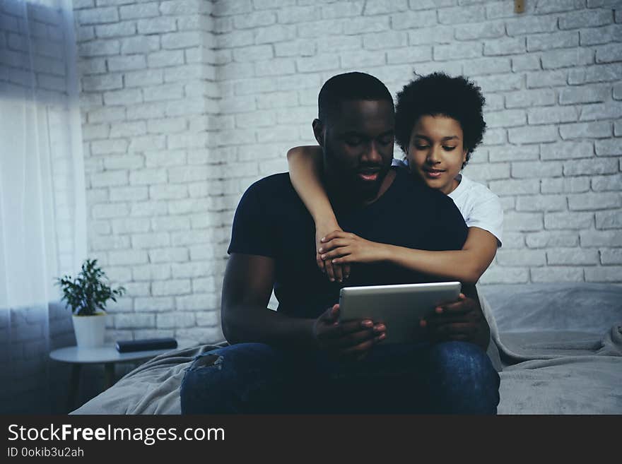 African American boy hugging father who interacts with pc tablet. Child education concept. Fatherhood