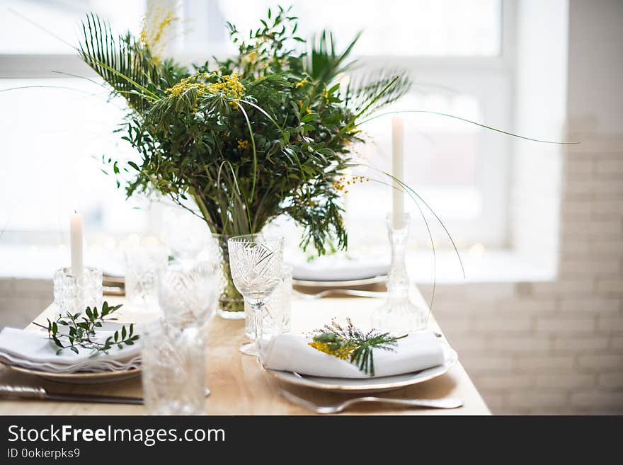 Beautiful springtime table setting with green leaves and mimosa branches, bright white table dinner decoration