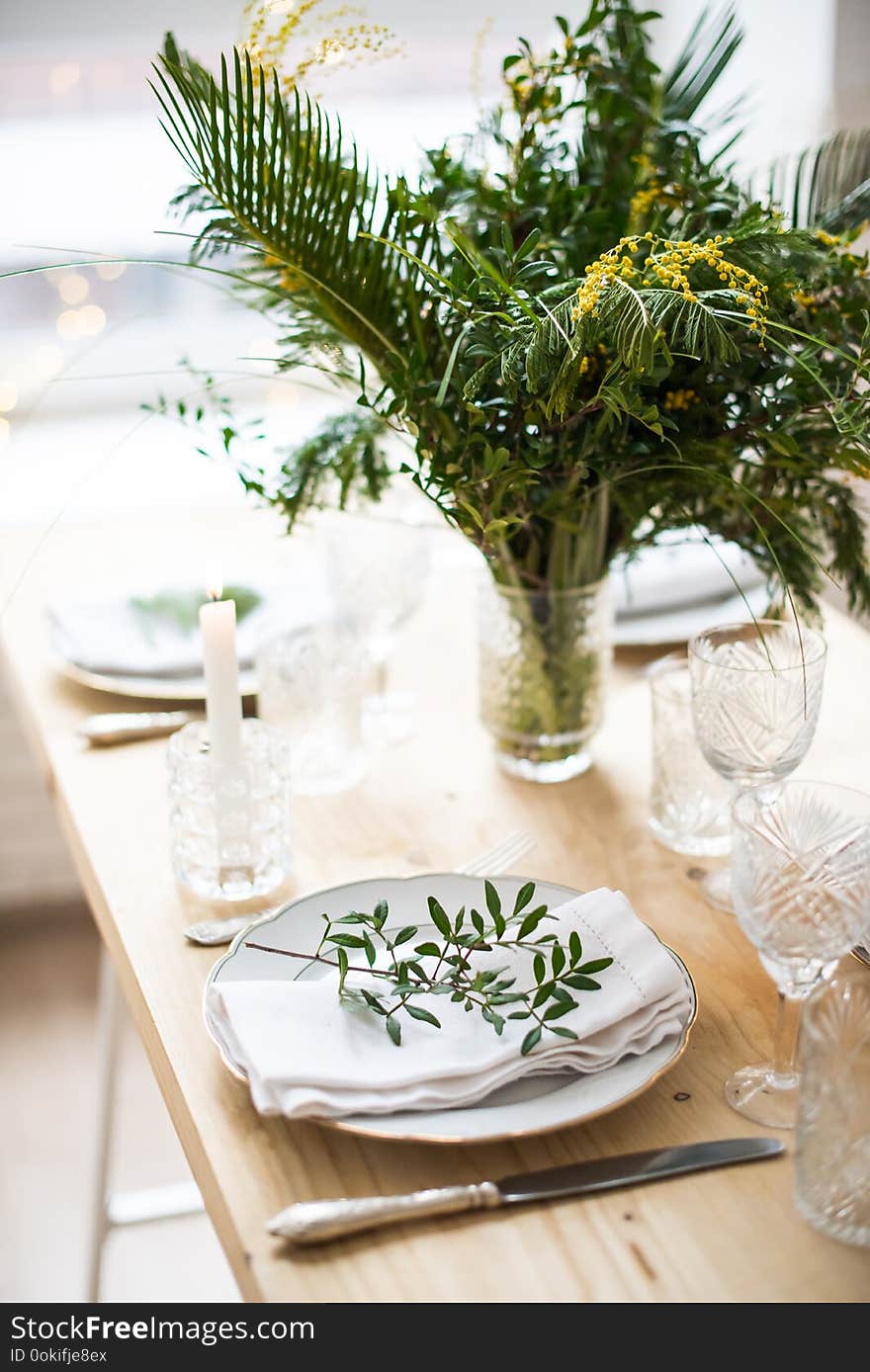 Beautiful springtime table setting with green leaves and mimosa branches, bright white table dinner decoration close-up