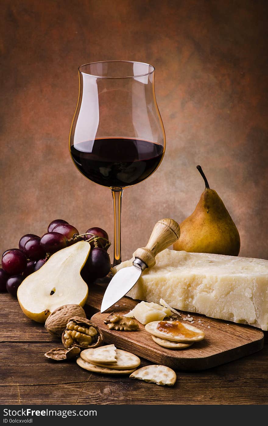 Still life. Meal with Parmesan cheese, crackers with jam, fresh fruit, a glass of red wine and some walnuts on rustic wooden table. Still life. Meal with Parmesan cheese, crackers with jam, fresh fruit, a glass of red wine and some walnuts on rustic wooden table