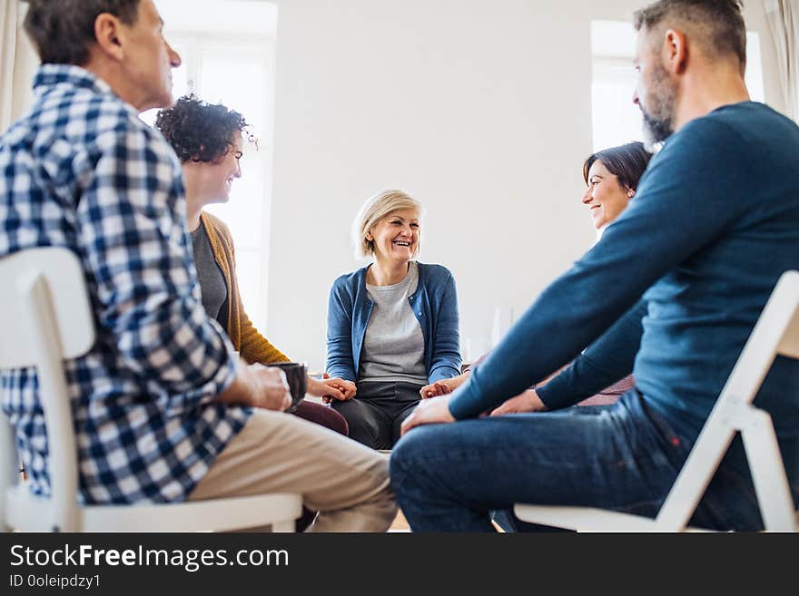 Men and women sitting in a circle and holding hands during group therapy, laughing.