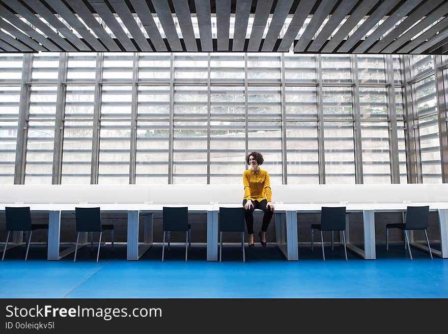 A portrait of a young student or businesswoman sitting on desk in room in a library or office.