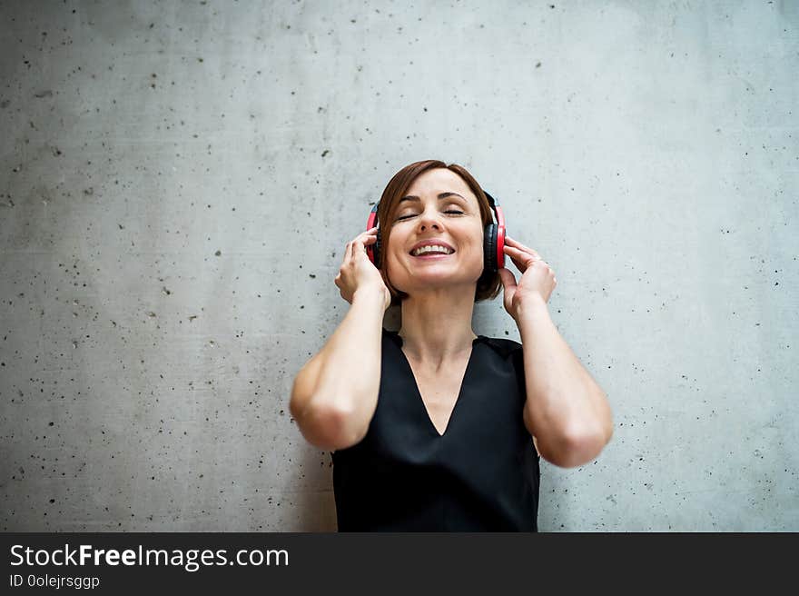 Young business woman with headphones standing against concrete wall in office.