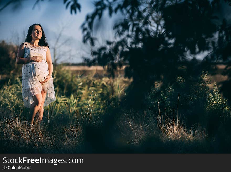 Pregnant girl at sunset in a loose dress in nature alone