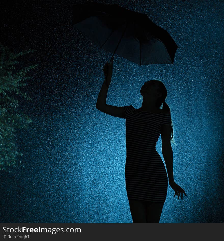 Silhouette of the figure of a young girl with an umbrella in the rain, a young woman with hand-picked hair is happy to drops of water, concept weather and mood